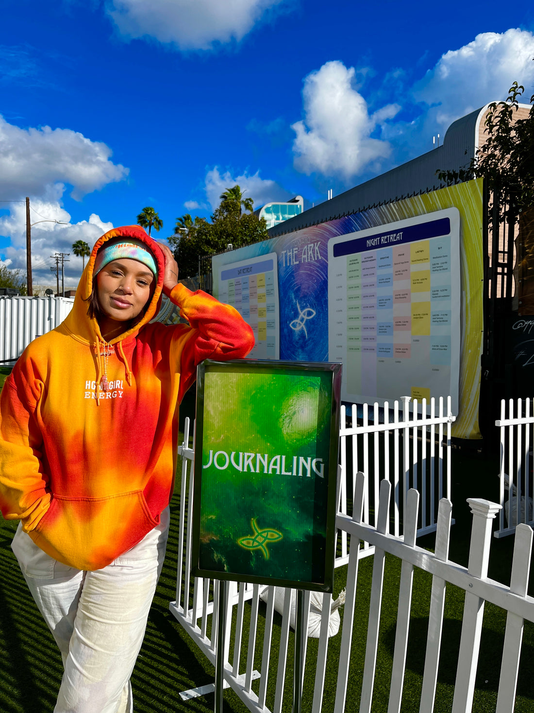Felicia in the orange Homegirl Energy hoodie leaning on a green sign that says "Journaling" at The Ark